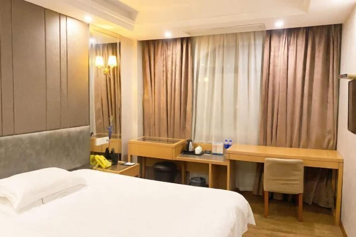 Una habitación de hotel con cama, escritorio, silla, espejo y cortinas.