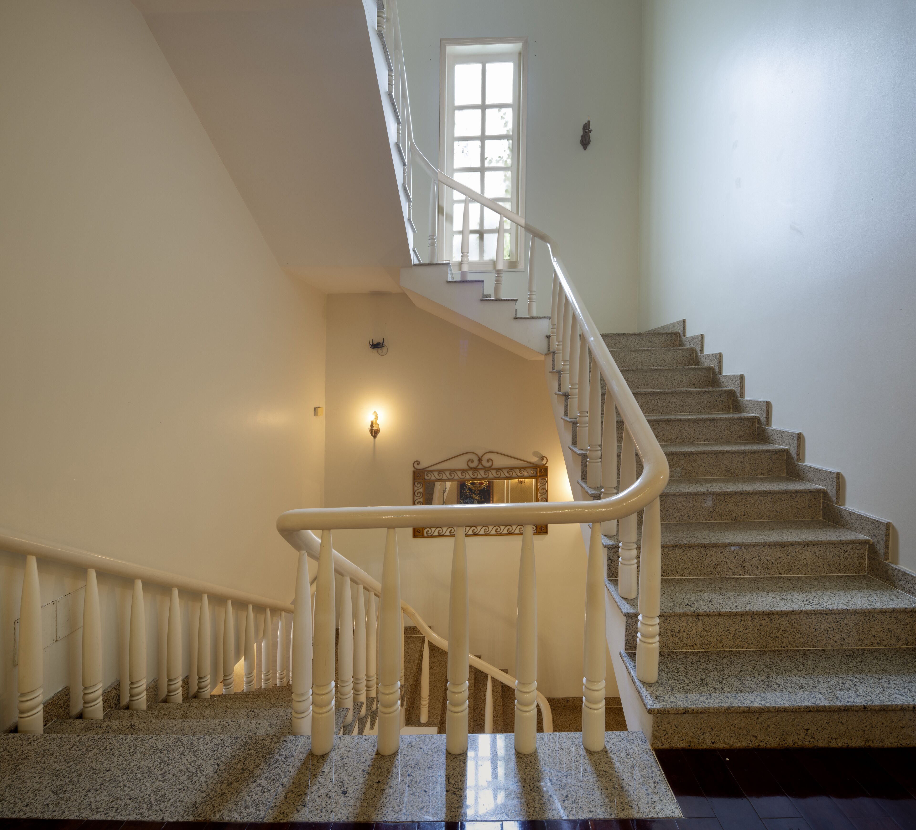 A grand staircase with a white handrail, granite steps, and a small window at the top.
