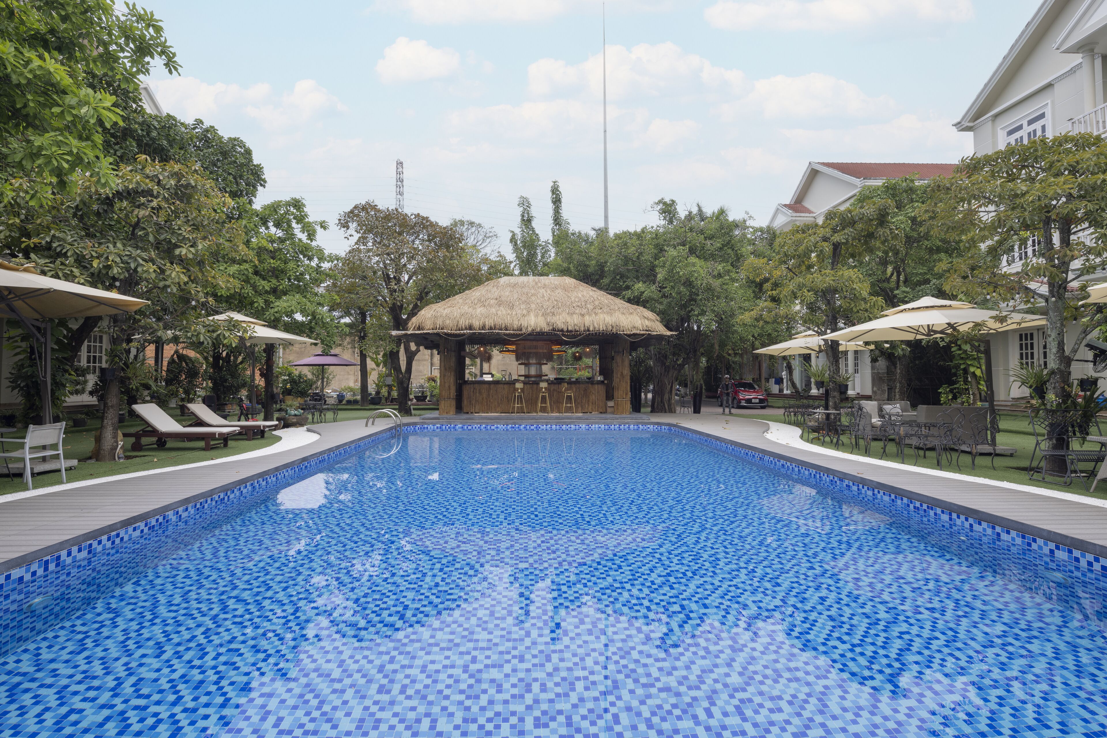 Una piscina con sillas de descanso y sombrillas, rodeada de árboles y edificios.