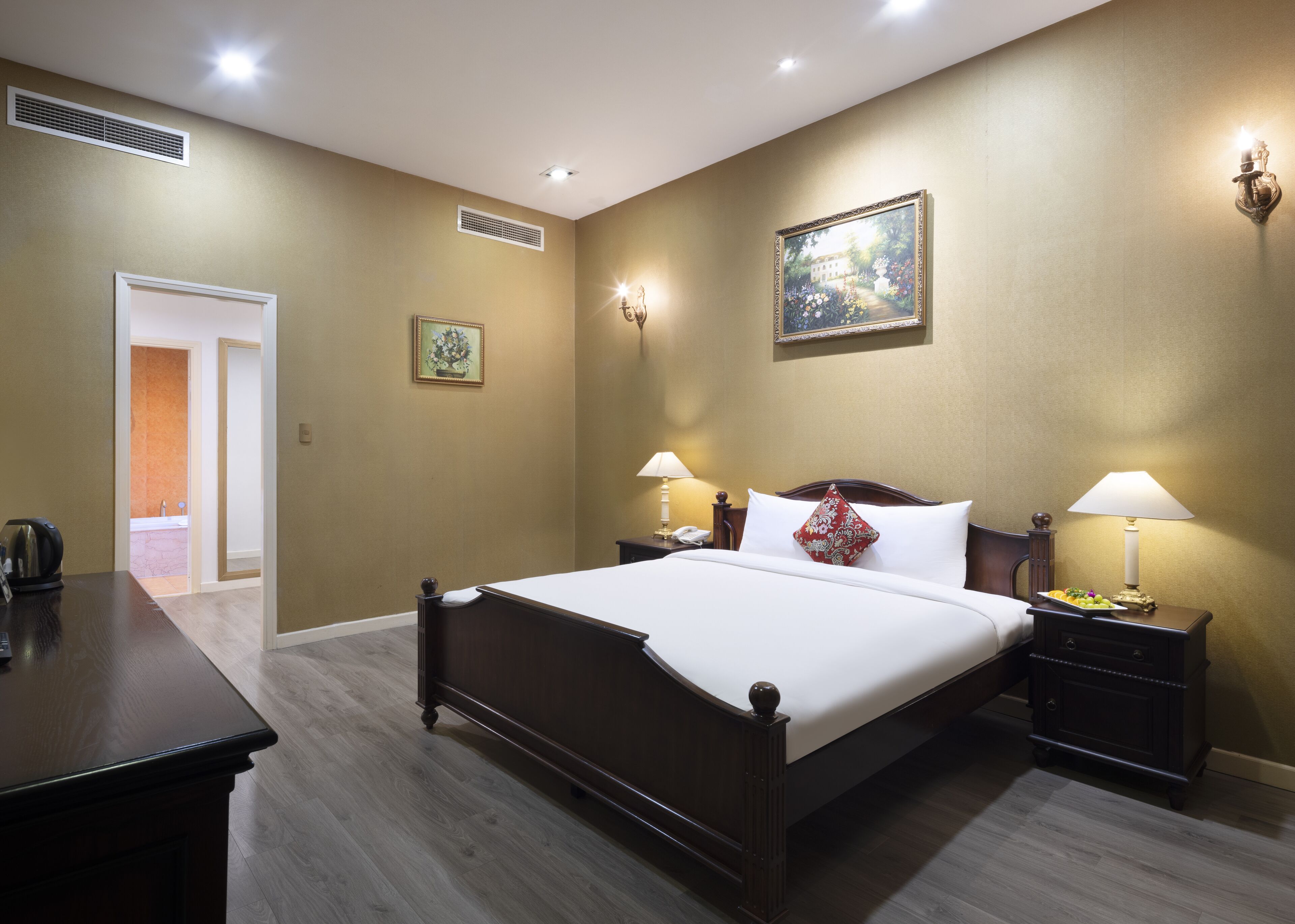 Habitación de hotel con una cama grande, mesitas de noche con lámparas, un cuadro en la pared y una puerta que da a un baño.