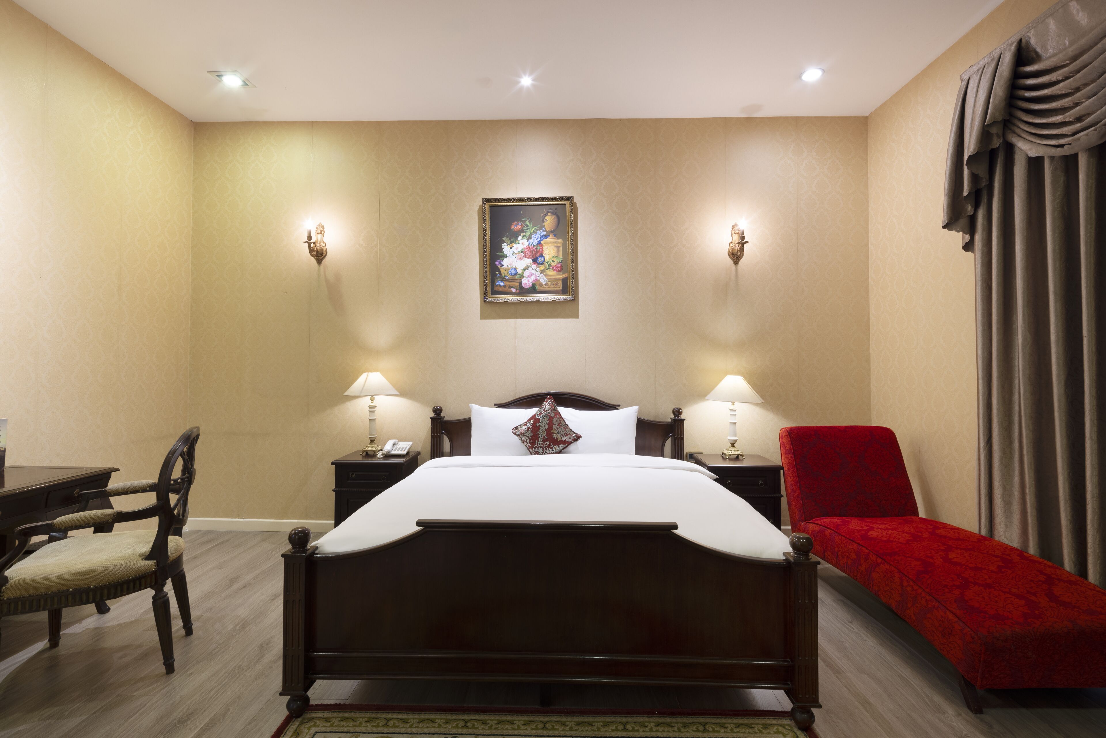 A hotel room with a wooden bed, two bedside tables with lamps, a red chair, a desk, and a patterned wall.