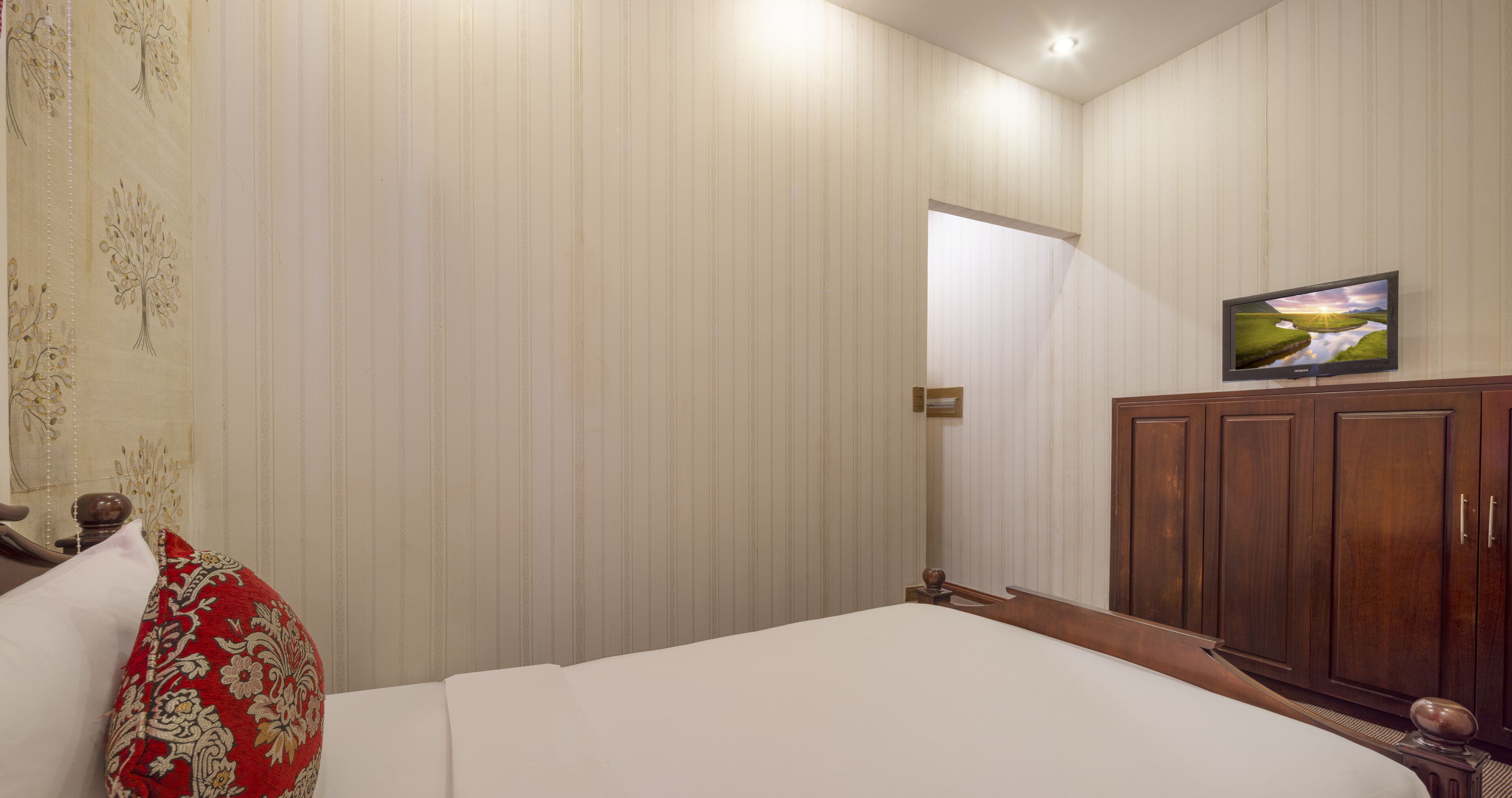 Une chambre d’hôtel avec un lit, un téléviseur fixé au mur et une armoire en bois.