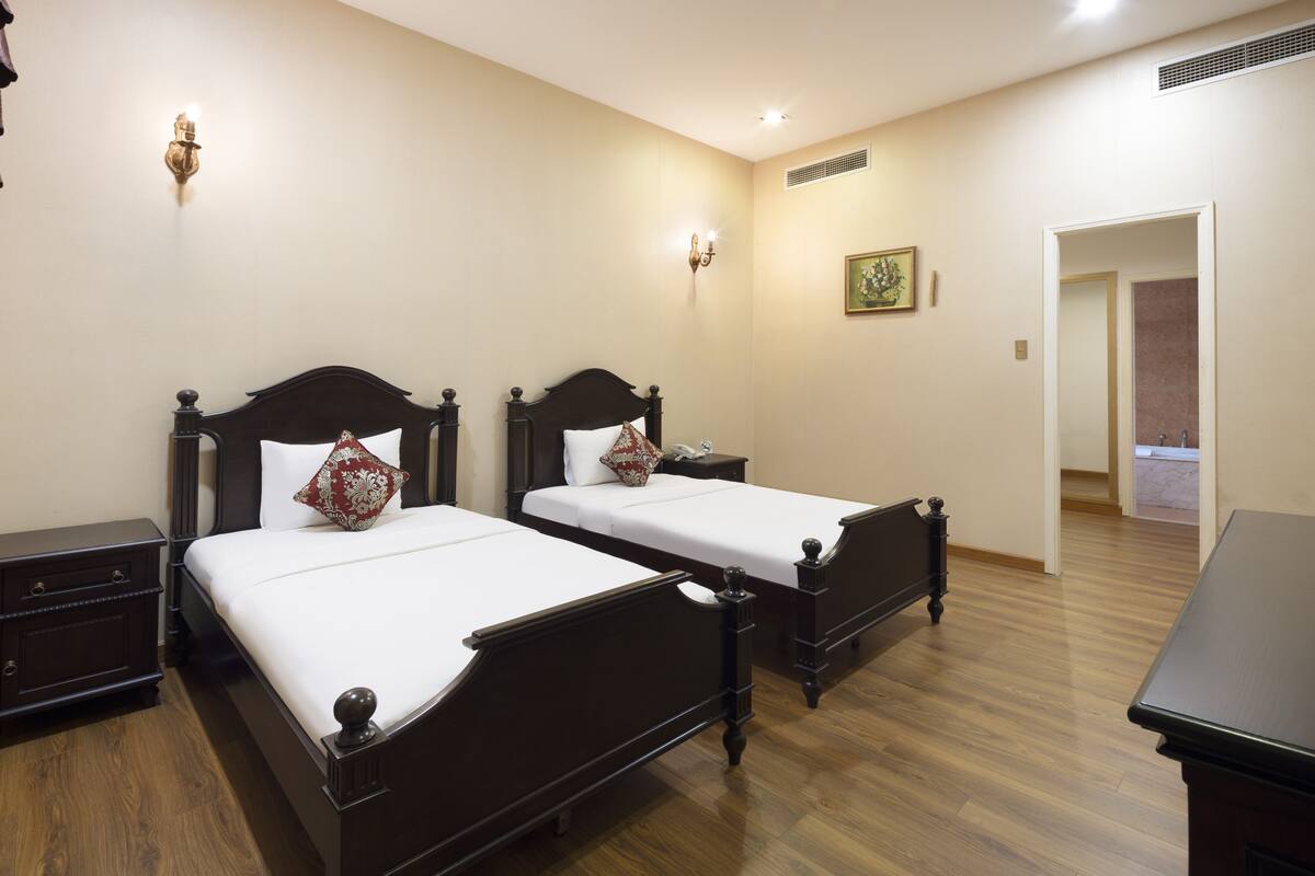 Een hotelkamer met twee houten bedden, een nachtkastje, een dressoir en een badkamer die door een open deur zichtbaar is.
