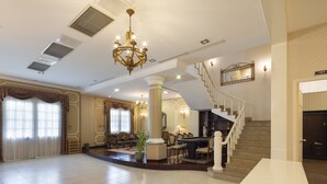 A spacious lobby with a grand staircase, a chandelier, and a billiards table.