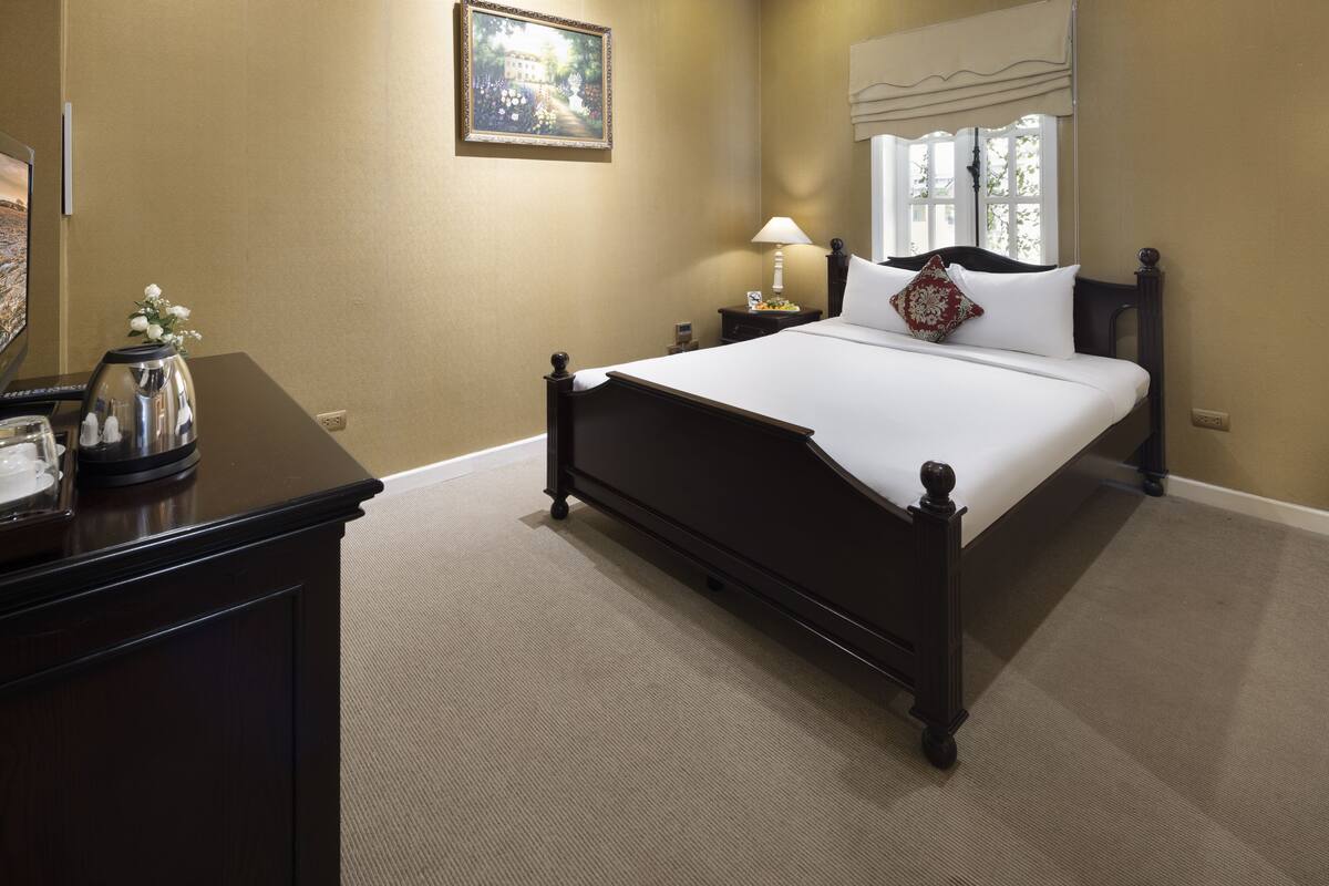 Een keurig opgemaakt slaapkamer met een bed, nachtkastje, lamp en een decoratieve vaas.
