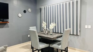 A dining area with a gray wall, a TV mounted above a shelf, and a window with vertical blinds.