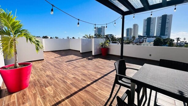 A rooftop terrace with wooden flooring, potted plants, a table and chairs, and string lights.