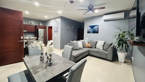 A modern living room with a grey sofa, a dining table with a vase of flowers, and a ceiling fan.
