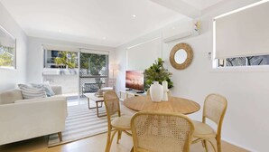 Un salon moderne avec une table de salle à manger ronde, des chaises en osier, un canapé blanc et un téléviseur.