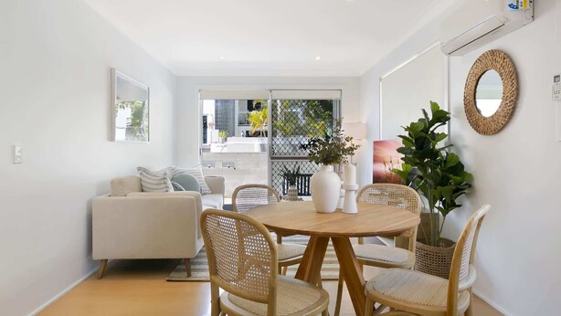 Un salon moderne avec un canapé blanc, une table de salle à manger ronde en bois et des chaises en osier.