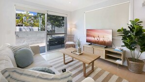 Un salon moderne avec un canapé, une table basse, un téléviseur et une vue à travers une porte vitrée.