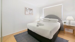 Une chambre à coucher moderne, avec un lit, des tables de chevet, une lampe de chevet, un tableau accroché au mur et un luminaire au plafond.