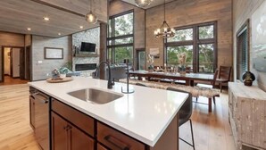 A spacious kitchen with a large island, wooden cabinetry, and a stone backsplash. There are large windows providing natural light and views of the outdoors. - Take A Dip Lodge - Indoor Heated Pool (Sevierville)
