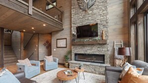 A spacious living area with a stone fireplace, a television mounted on the wall, and a staircase leading to an upper level. - Take A Dip Lodge - Indoor Heated Pool (Sevierville)