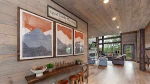 A spacious living area with a wooden ceiling, a large window, and a bar area with stools. - Take A Dip Lodge - Indoor Heated Pool (Sevierville)