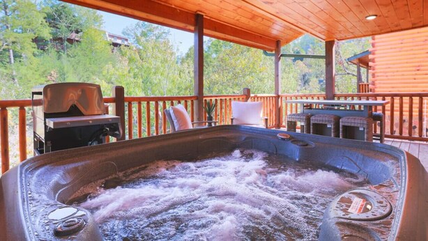 A hot tub with a wooden deck and outdoor seating, surrounded by trees. - Indoor Pool Cabin, Theater, 7 mi to Dollywood (Pigeon Forge)
