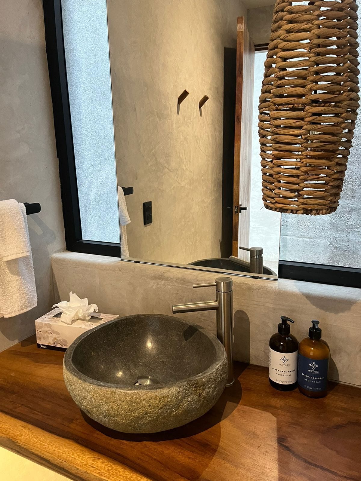 A modern bathroom with a stone sink, wooden countertop, and a large mirror.
