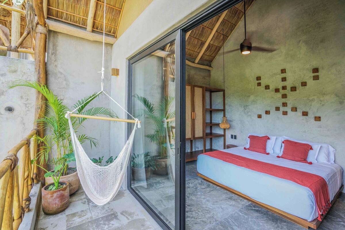 Un dormitorio con cama, una silla colgante y plantas en macetas.