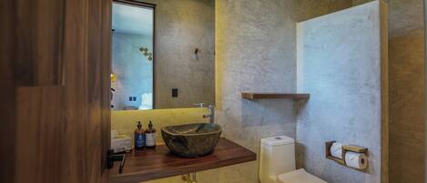 A bathroom with a wooden vanity, a stone sink, a toilet, and a towel rack.
