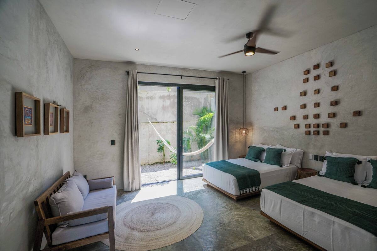 Un dormitorio moderno con dos camas, una hamaca y un ventilador de techo.