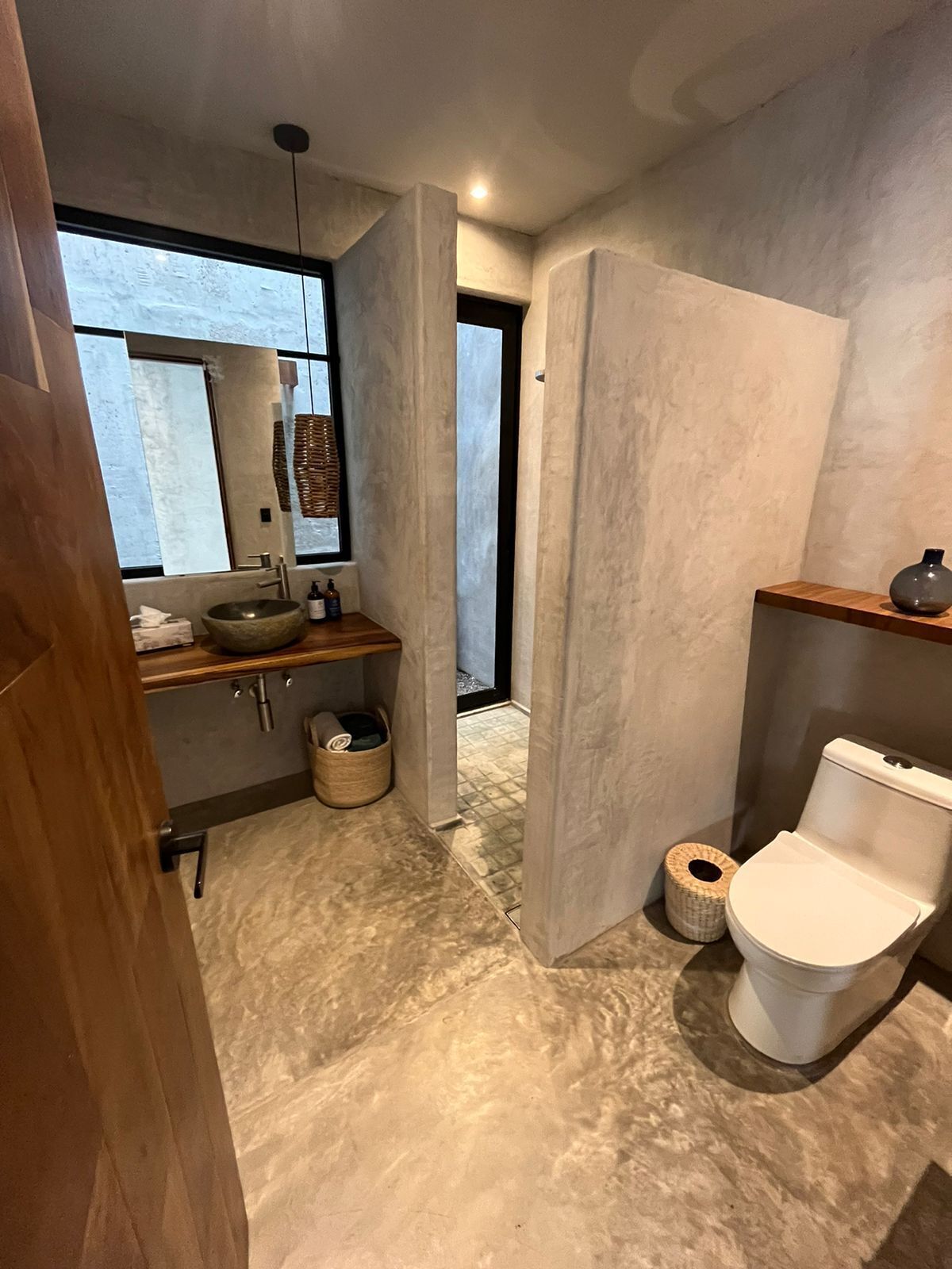 A modern bathroom with a large mirror, a round sink, a toilet, and a wooden shelf.