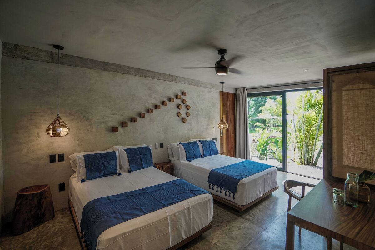 Un dormitorio con dos camas, ventilador de techo y vistas a la vegetación exterior.