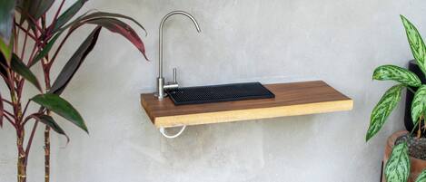 A wall-mounted sink with a wooden shelf, a metal faucet, and two potted plants.