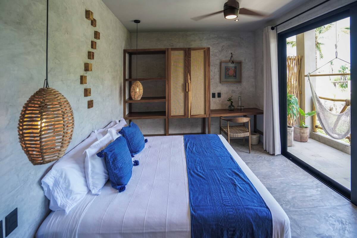 Un dormitorio con una cama grande, un escritorio y una hamaca junto a la ventana.