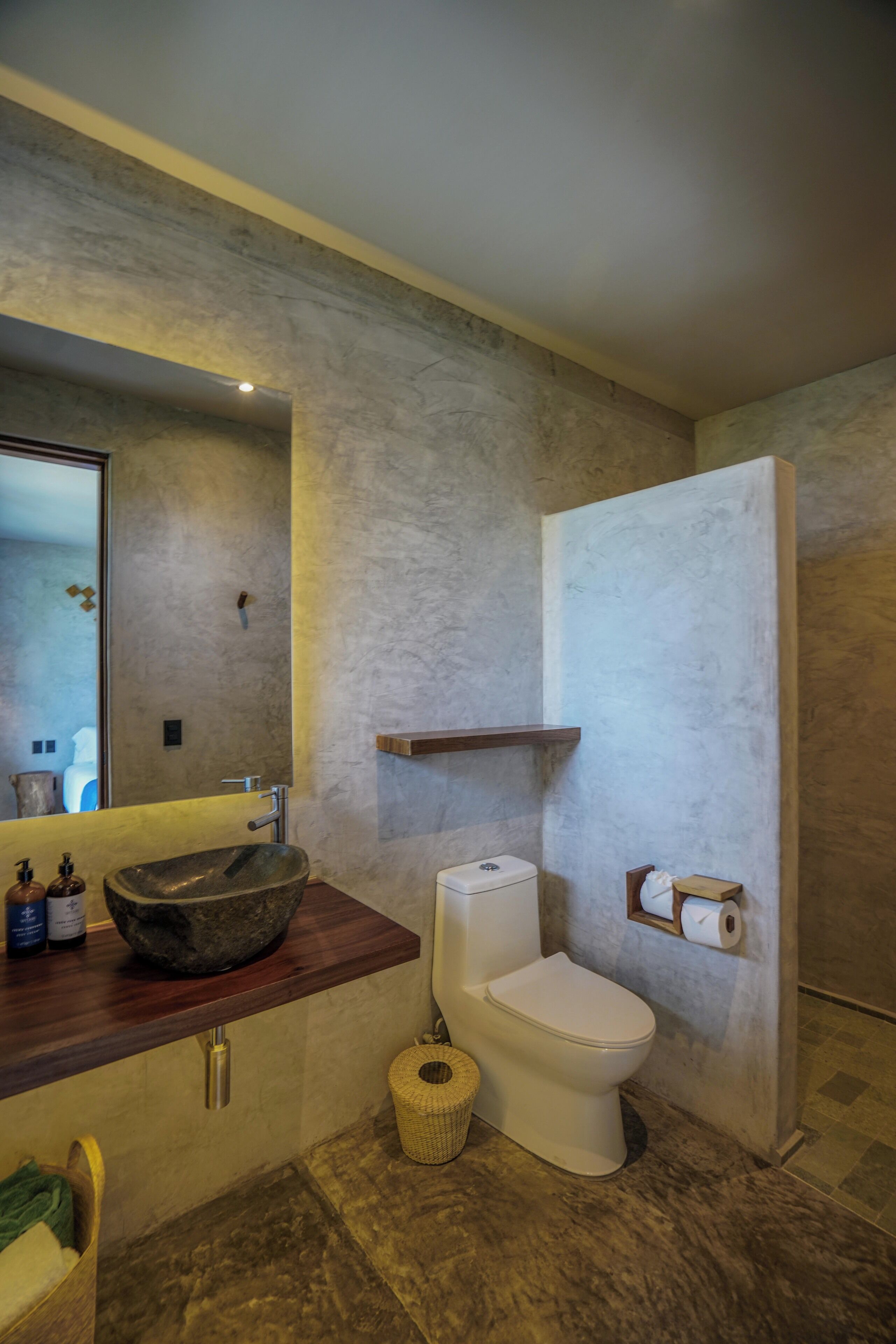 A bathroom with a stone sink, a toilet, and a mirror.