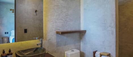 A bathroom with a stone sink, a toilet, and a mirror.