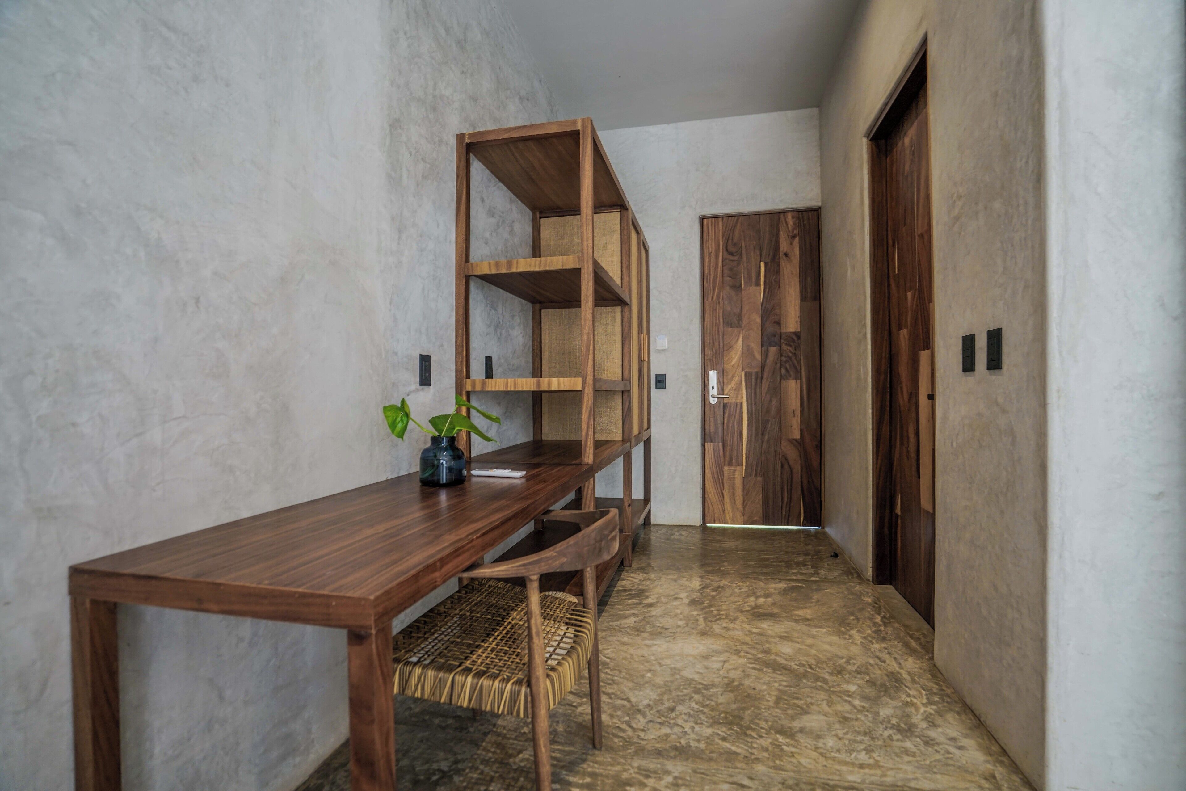 A hallway with a wooden table, wicker chair, and a wooden shelving unit.