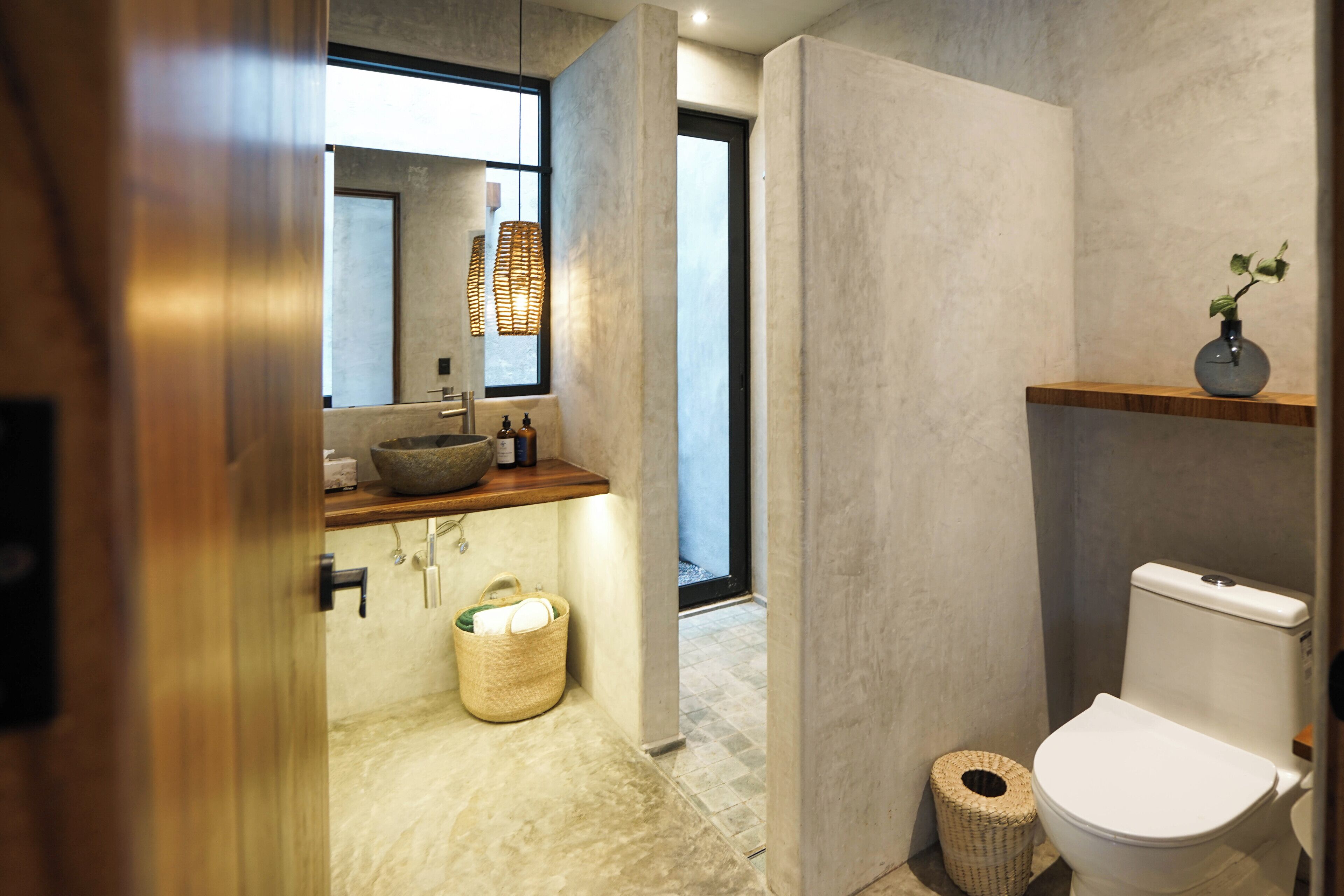 Ein modernes Badezimmer mit großem Fenster, einem Steintonne, Toilette und einer kleinen Ablagefläche mit Pflanze.