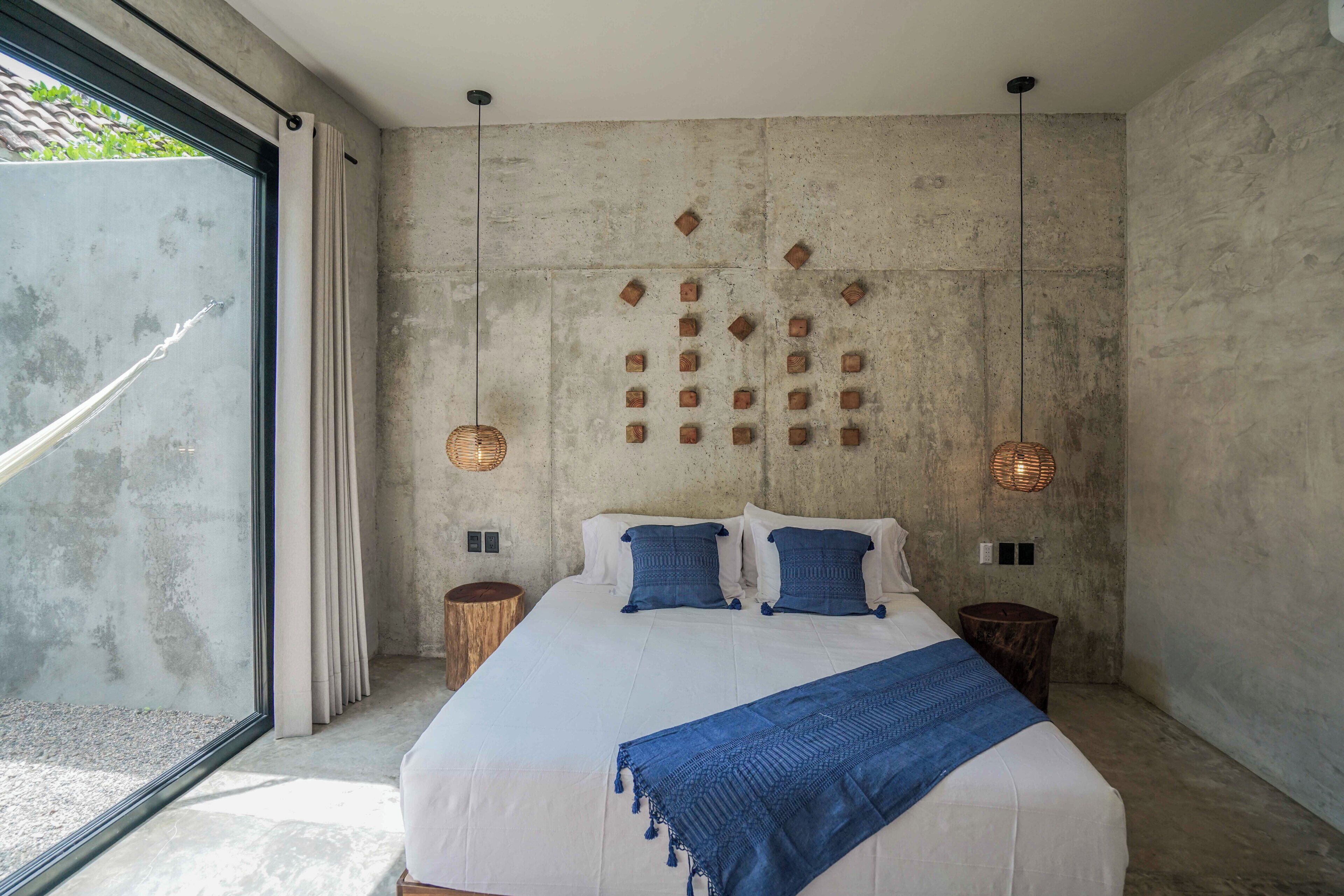 A bedroom with a large bed, a concrete wall, and a view through a glass door.