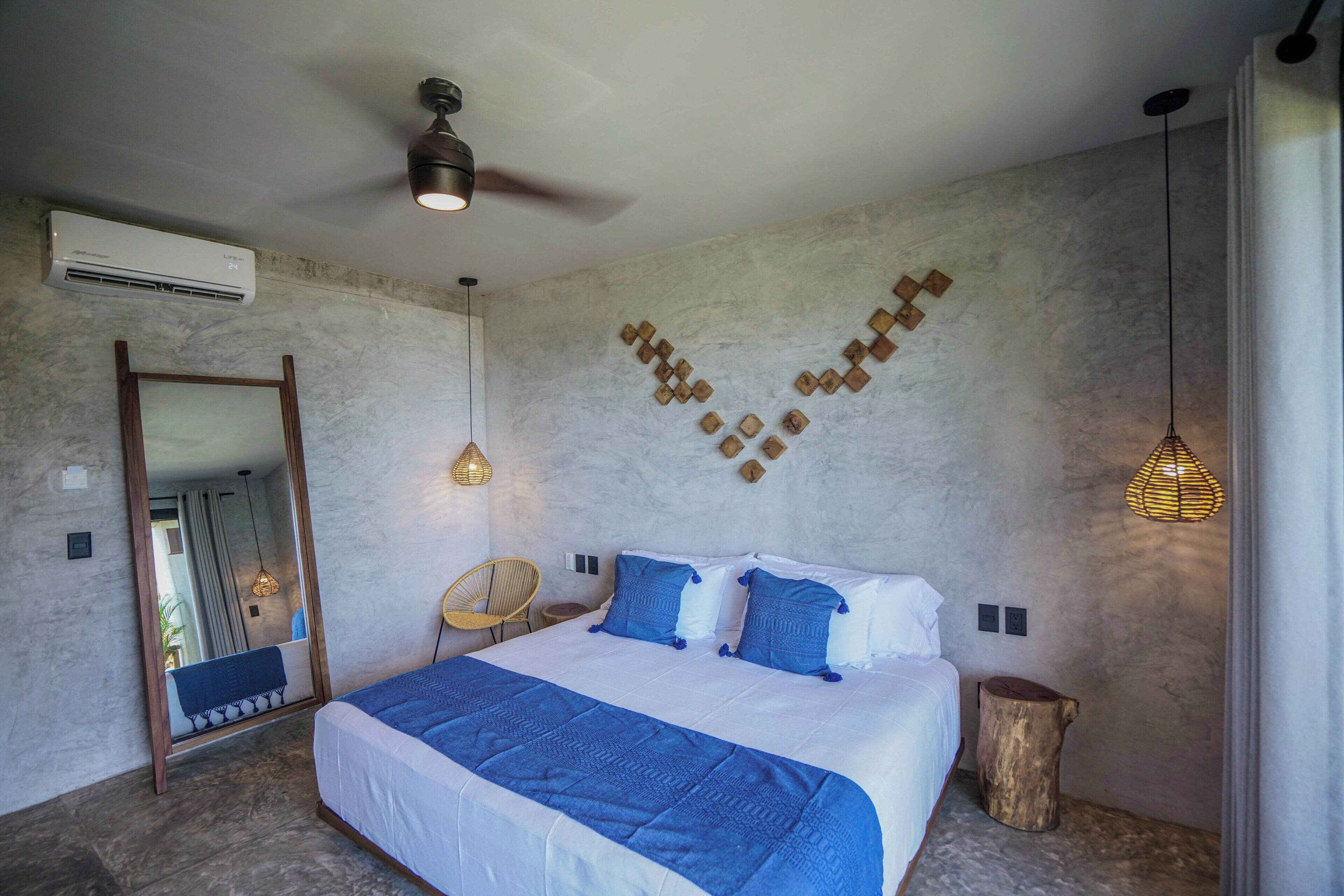 Ein Schlafzimmer mit einem großen Bett, einem Deckenventilator, einer Klimaanlage, einem Spiegel, einem Holzstuhl und einer Wandleuchte.