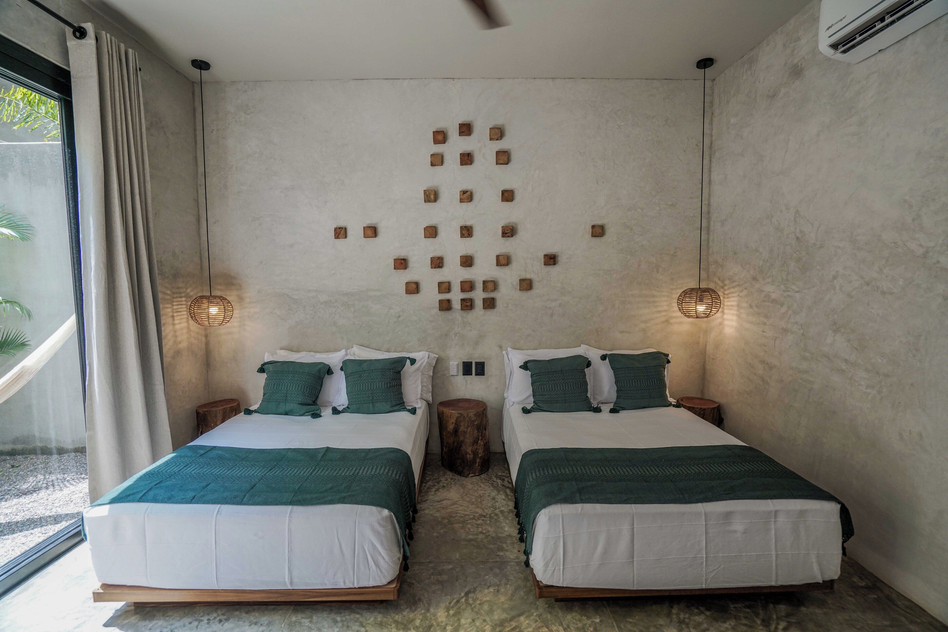 Une chambre avec deux lits, un plancher en bois, un mur orné d’un motif géométrique et une fenêtre avec des rideaux.
