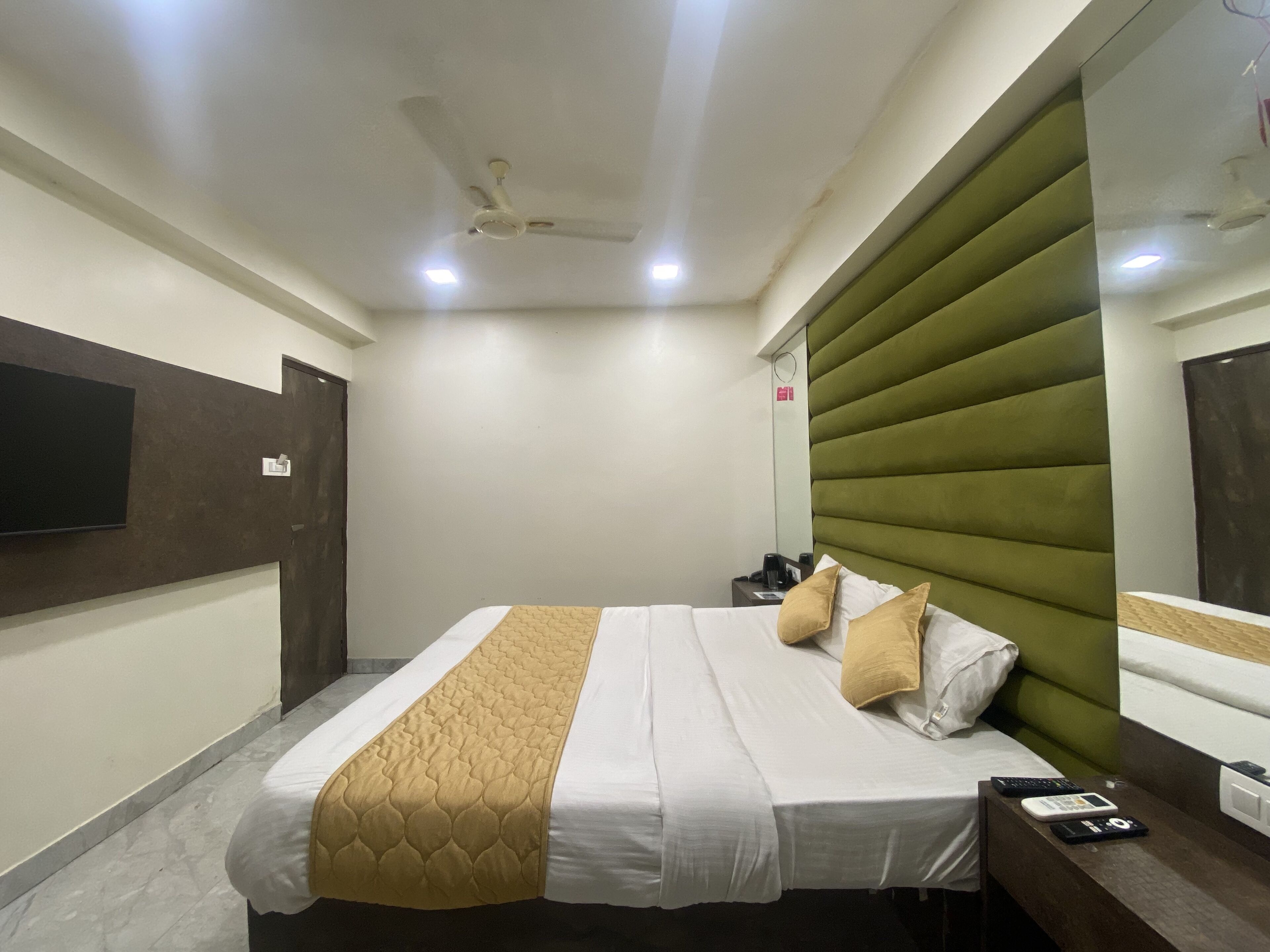 A hotel room with a bed, a bedside table, a TV mounted on the wall, and a ceiling fan.