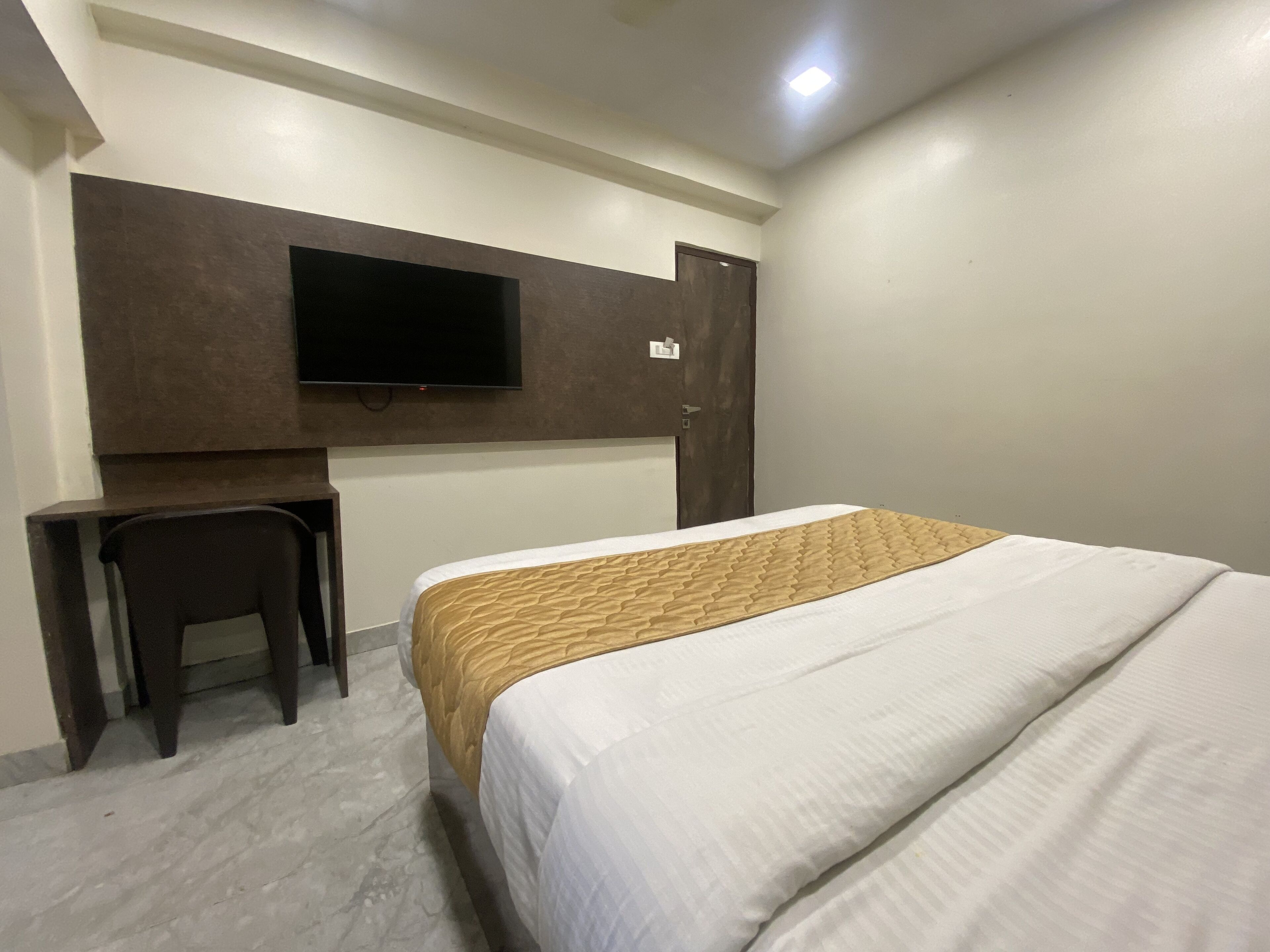 Une chambre d’hôtel équipée d’un lit, d’un bureau, d’une chaise, d’un téléviseur fixé au mur et d’une porte.