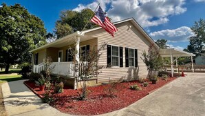 A single-story house with a porch, a flag, and a red flower bed.