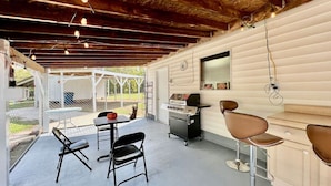 A covered outdoor area with a grill, two bar stools, and a table with chairs.