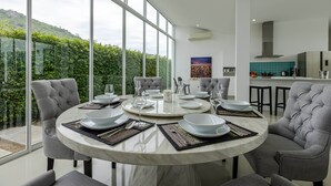 A modern dining area with a round table set for six, surrounded by grey upholstered chairs. - Modern 4 Bedroom Pool Villa - KHA5 (Hua Hin)
