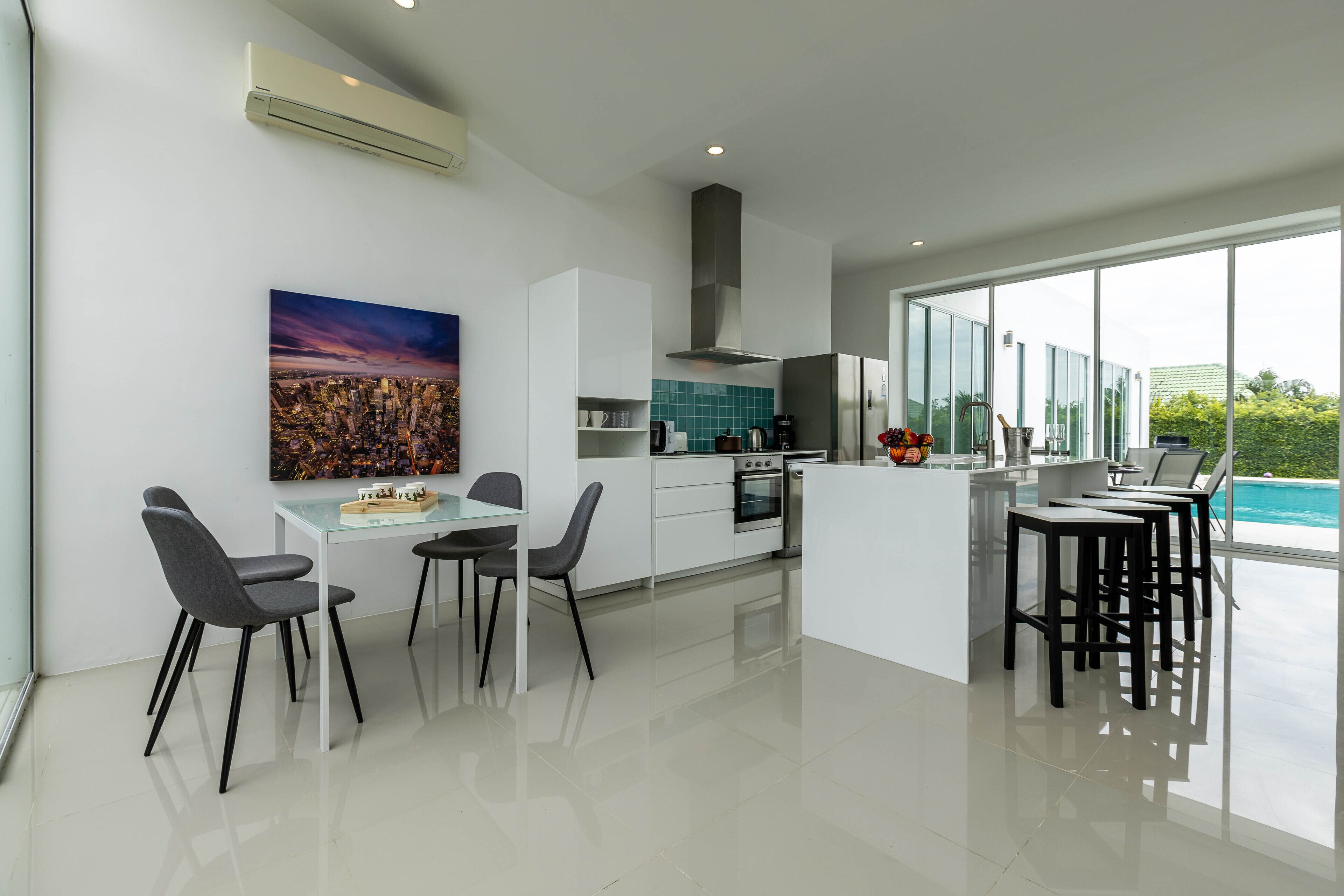 A modern kitchen with a dining area, large windows, and a view of the outdoors.