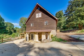 A rustic wooden cabin with a stone foundation, a porch with curtains, and a clear view of the surrounding forest.