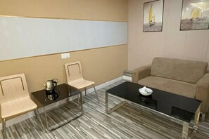 A modern living room with a beige sofa, a glass coffee table, and two chairs. There are framed pictures on the wall. - Yiru Express Apartment Hotel（Shantou's long corridor on the seaside) (Shantou)
