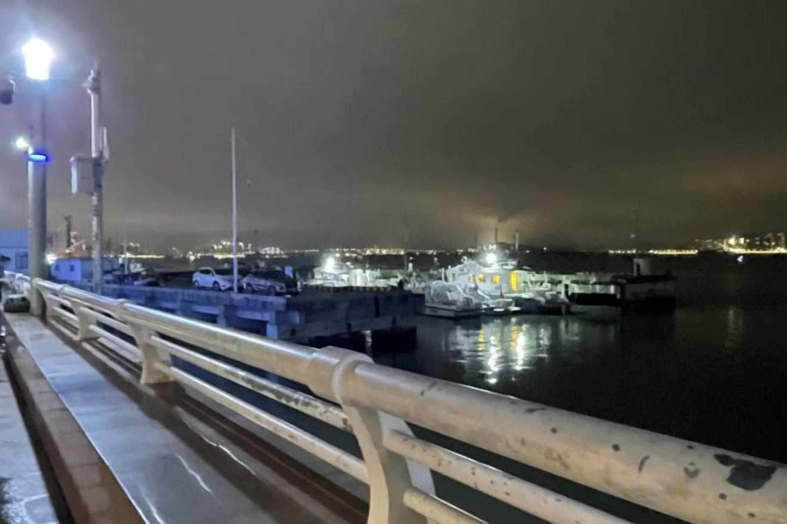 A nighttime view of a waterfront with a railing, a dock, and boats.