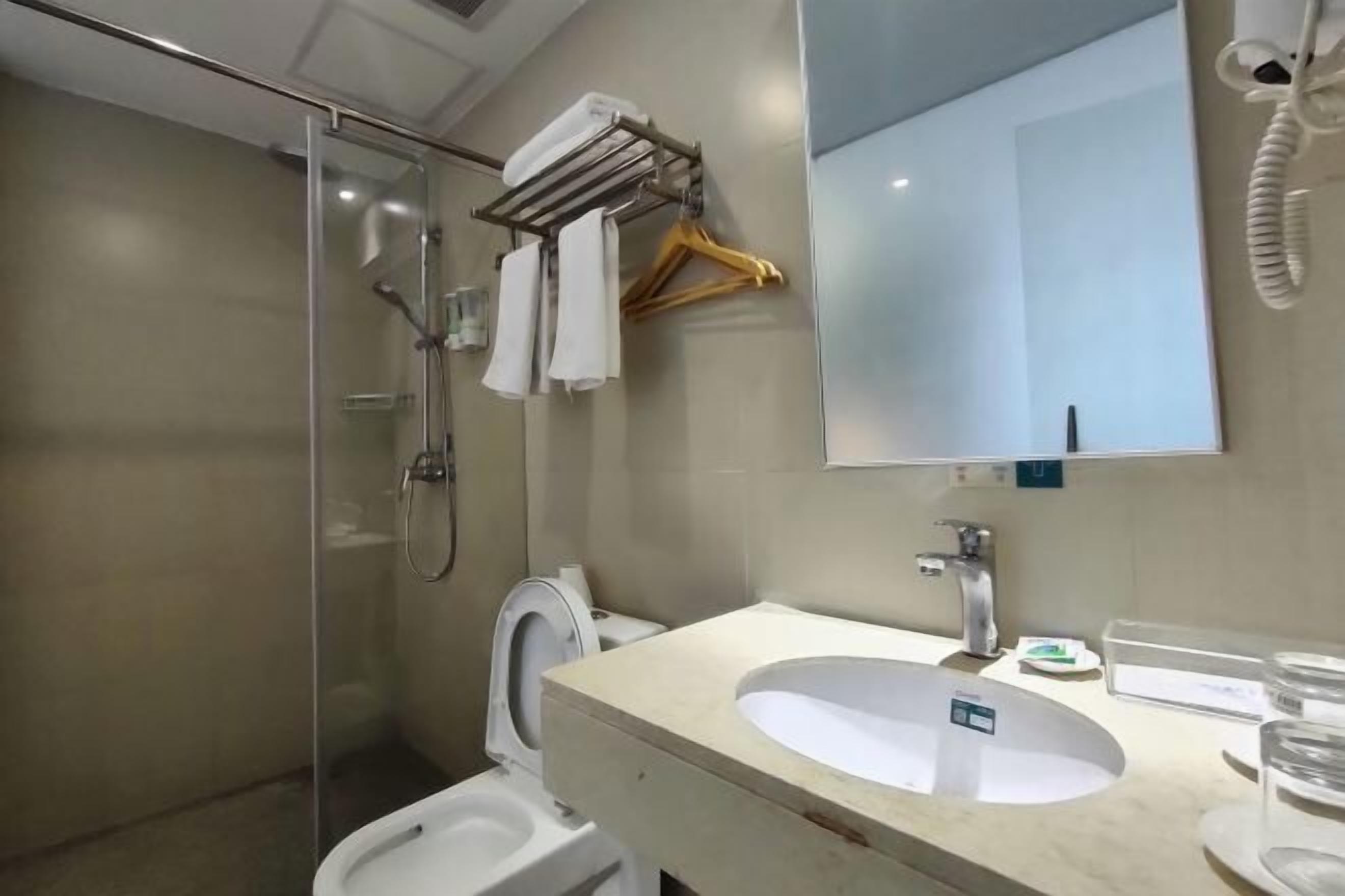 A bathroom with a glass shower enclosure, a toilet, a sink with a mirror, and a towel rack with hangers.