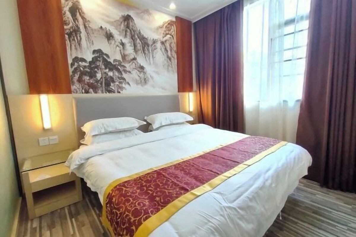 A hotel room with a bed, nightstand, wall art, and a window with curtains.