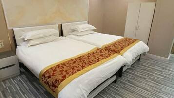 A hotel room with two beds, a wardrobe, and a marble headboard.