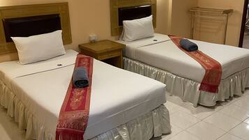Habitación de hotel con dos camas, cada una con cubrecolchón blanco y un corredor decorativo rojo. Entre las camas hay una mesita de noche con una lámpara, y un cuadro de caballos en la pared.