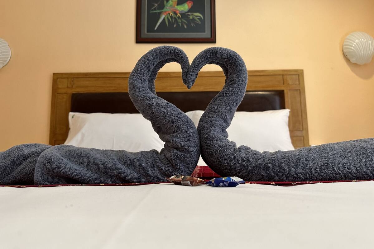 Een bed met een handdoek in de vorm van een hart en een ingelijste foto aan de muur.