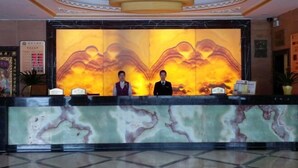 A hotel reception area with a marble counter, two receptionists, and a large wall mural. - Fulin Hotel (Huilai)